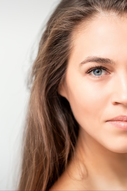 Half face portrait of young caucasian woman with natural make up and eyelash extensions  on white wall