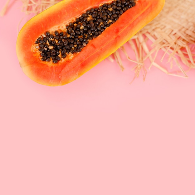 Half a fresh papaya and a straw hat on a pink background.