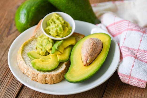 Half gesneden avocado en ondergedompelde avocadodip die op witte plaat wordt gepureerd