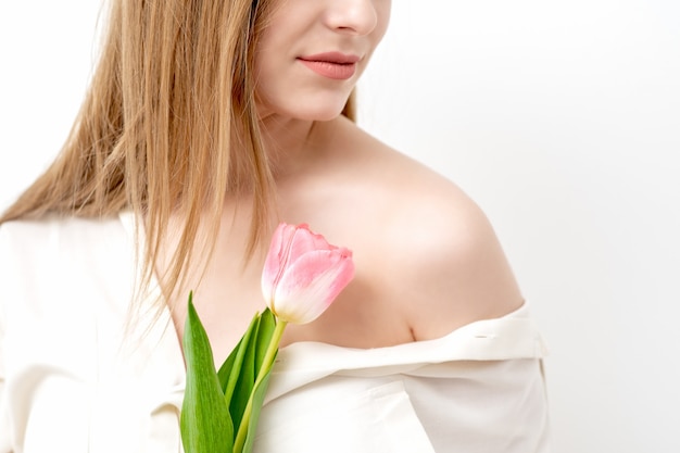 Half gezicht portret van een mooie jonge blanke vrouw met een roze tulp op witte achtergrond