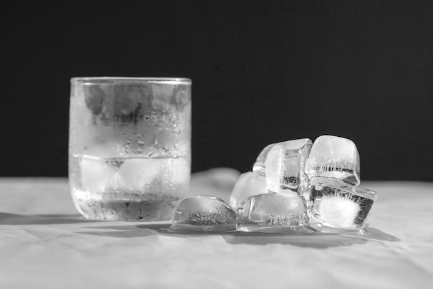 Half glas water met ijsblokjes en smeltende ijsblokjes bovenop tafel