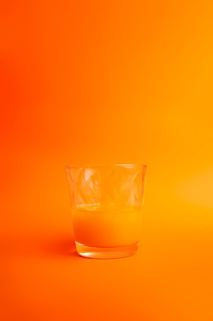 Half glass of orange juice on orange background