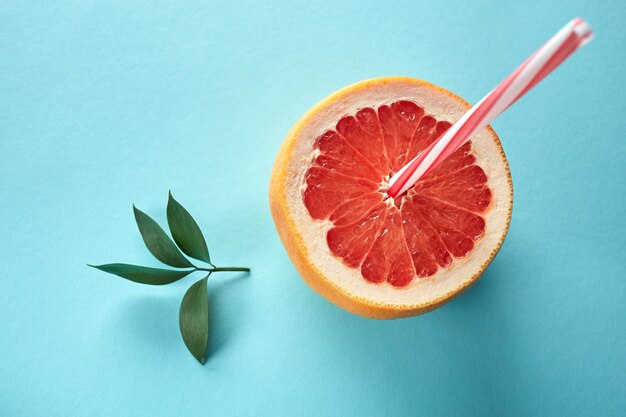 Half a grapefruit in the form of a glass with a drinking tube and a green leaf on a blue background