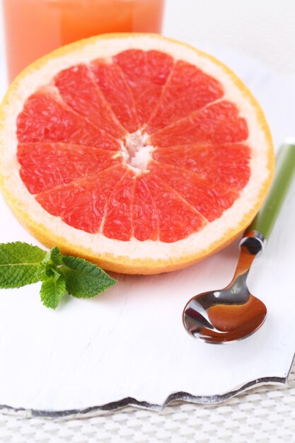 Half of grapefruit and spoon on wooden board on light background