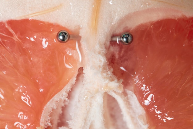 Half of grapefruit with vertical barbell piercing on a background