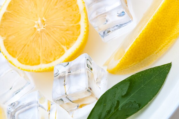 Half a juicy bright lemon with a green leaf and cubes of refreshing ice close up