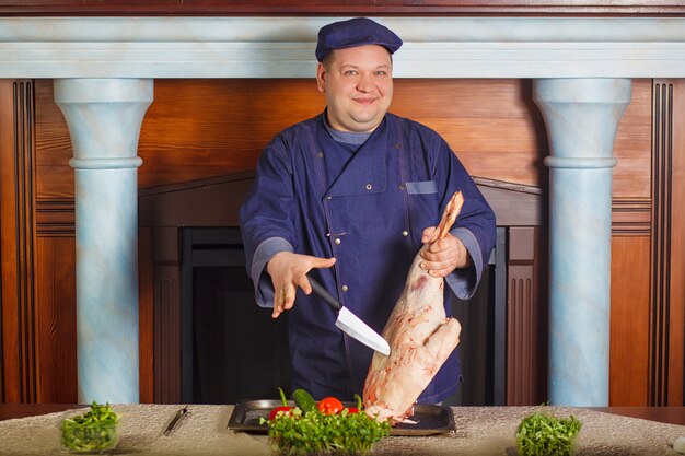 Half legth shot of thoughtful male chef, holds very big red raw piece of meat