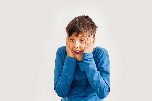 Half-length emotional portrait of caucasian teen boy wearing blue t-shirt. Surprised teenager looking at camera. Handsome happy child, isolated on white background.