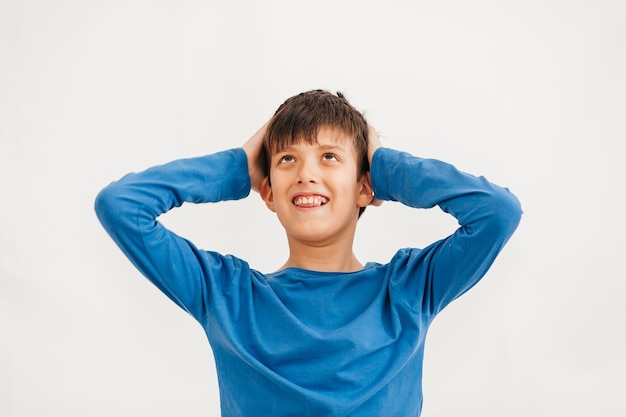 青いTシャツを着ている白人の10代の少年の半分の長さの感情的な肖像画。カメラを見て驚いたティーンエイジャー。ハンサムな幸せな子、白い背景で隔離。