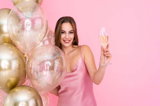 Half length of happy girl raises up glass of champagne stands near golden air balloons celebration