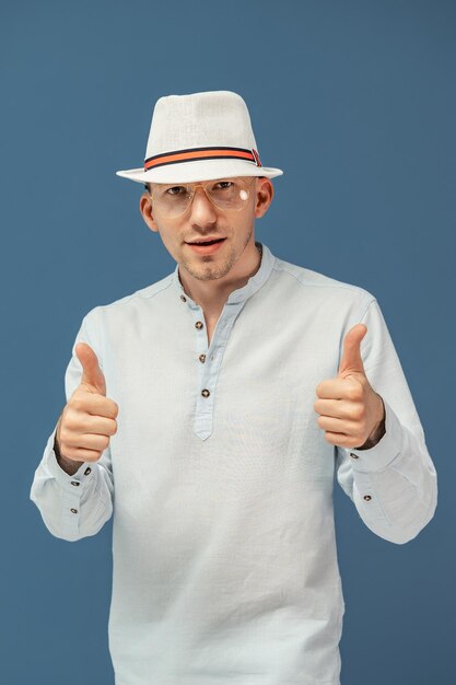 우아한 모자를 쓴 세련된 안경을 쓴 힙스터 남자의 절반 길이가 화려한 배경에서 엄지손가락을 치켜들고 있다