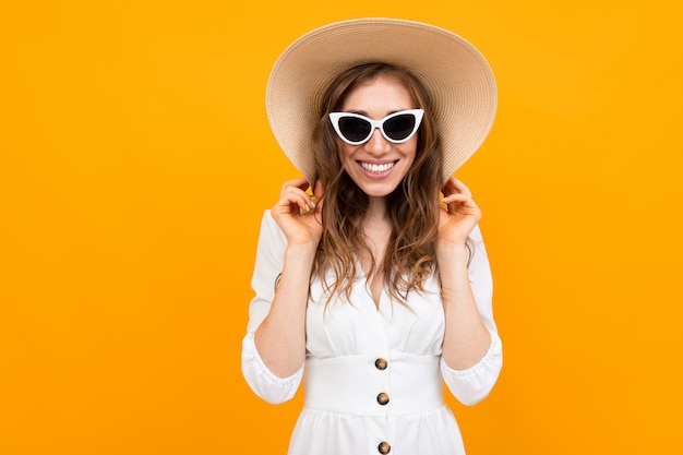 Half-length portrait of a girl in a hat and sunglasses on a surface of an orange wall