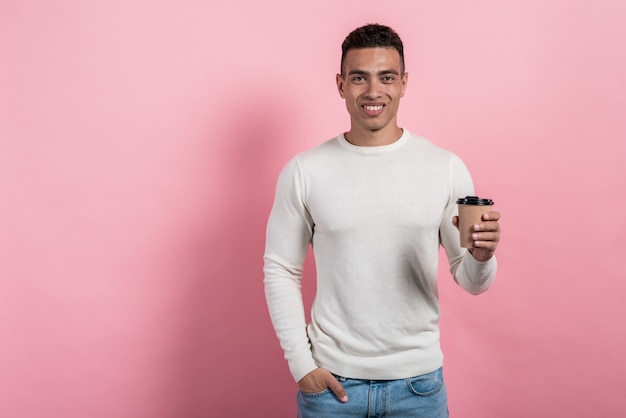 Half-length portrait of happy  mulatto man holding paper glass of coffee standing 