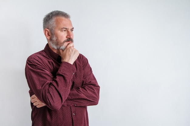 Half-length portrait of a serious gray-haired bearded man in a burgundy shirt on white