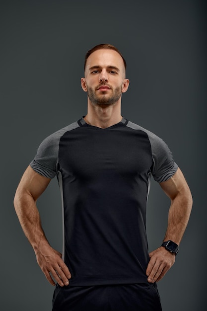 Half length portrait of young sporty guy in tshirt and shorts standing on gray studio background Serious millennial sportsman looking at camera Healthy lifestyle and sports concept
