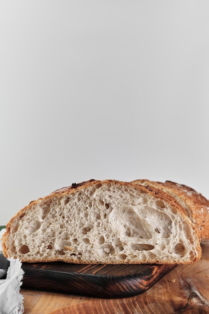 Mezza pagnotta di pane a lievitazione naturale artigianale su un tagliere cornice verticale in primo piano su sfondo grigio chiaro con spazio per la copia