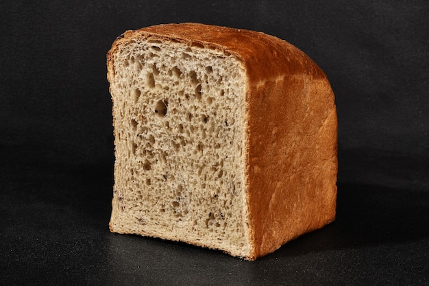 Half a loaf of fresh delicious baked gray bread against black background with copy space Closeup side view