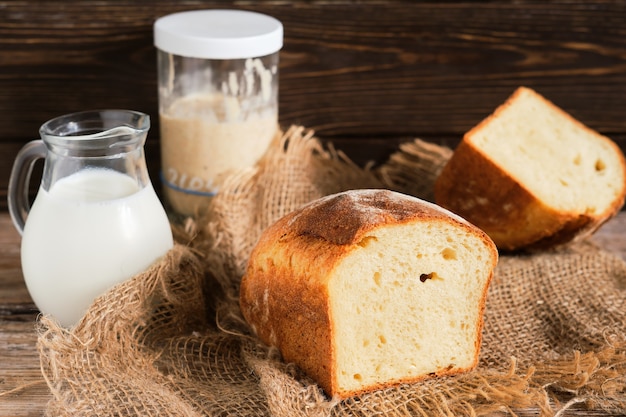 Mezza pagnotta di pane caseario a lievitazione naturale fatto in casa, fuoco selettivo. lievito naturale e una caraffa di latte sul tavolo. close-up, con copia spazio. pane artigianale su un rivestimento in tessuto, parete in legno