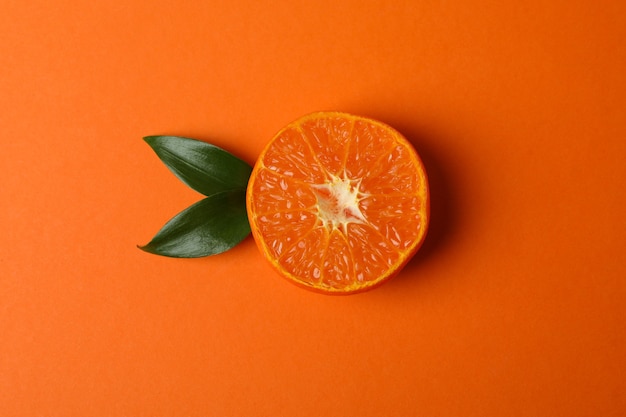 Половина мандарина с листьями на оранжевом столе