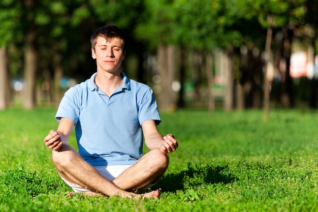 Half naakte man zittend op groen gras, mediteren en yoga pose te doen