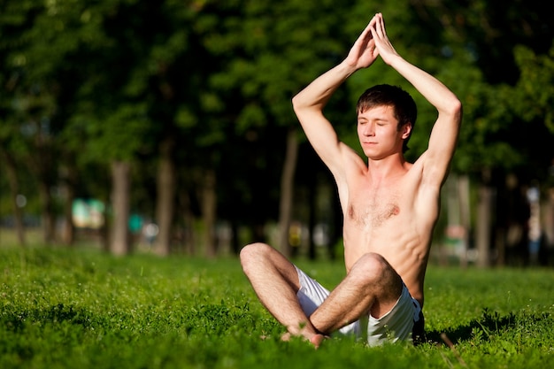 Half naakte man zittend op groen gras, mediteren en yoga pose te doen