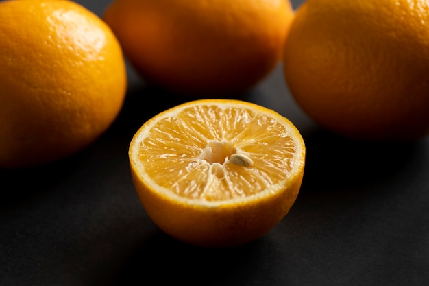 Half of the orange lies in front of the rest of the oranges. Ripe juicy yellow oranges on a black table