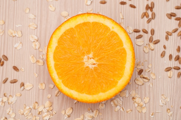 Photo half an orange on the table closeup with oatmeal and wheat on background