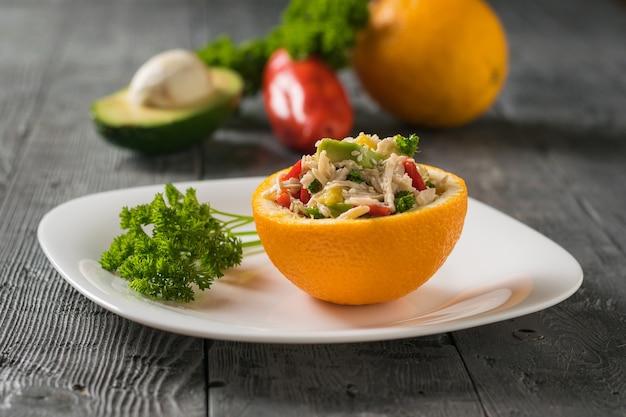 Half an orange with avocado salad and chicken with parsley on a white plate. Diet food of tropical fruits and chicken.