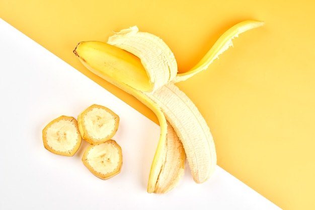 Фото Половина очищенного банана и ломтики на желтом белом фоне с копией пространства