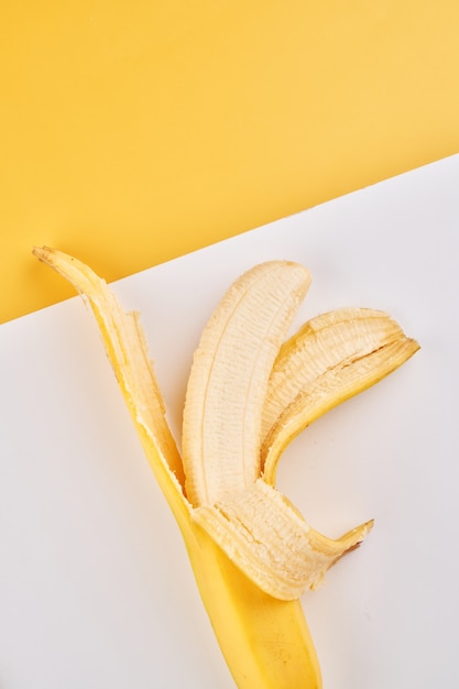 Foto banana mezza sbucciata su fondo bianco giallo con lo spazio della copia