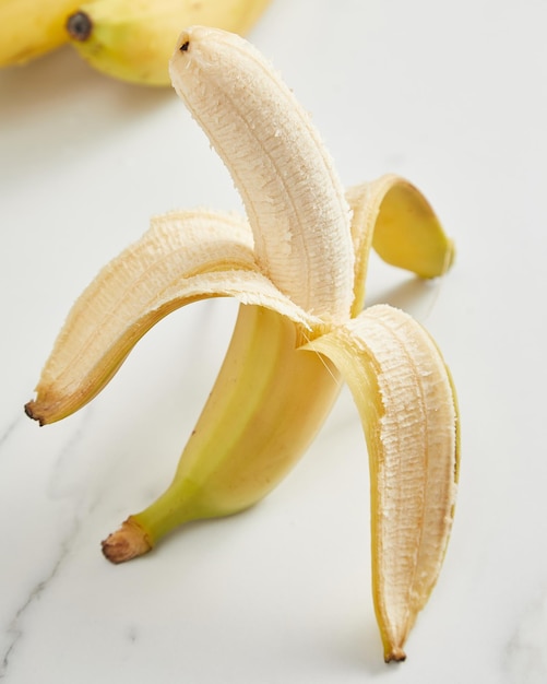 Half peeled ripe banana on white background