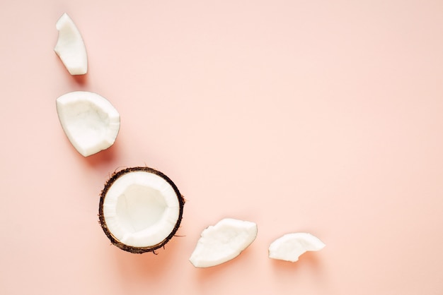 Half and pieces of coconut on a pink background