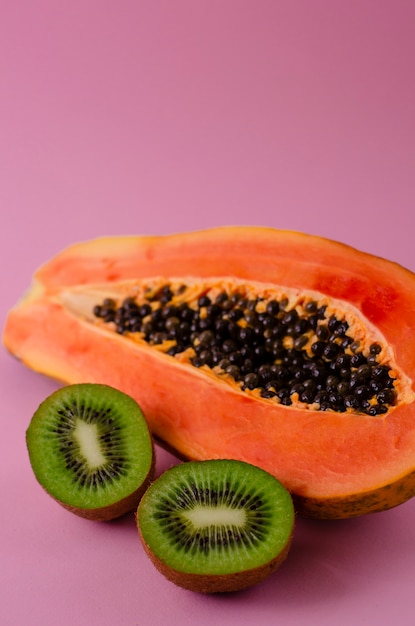 A half of ripe fresh papaya and kiwi on pink 