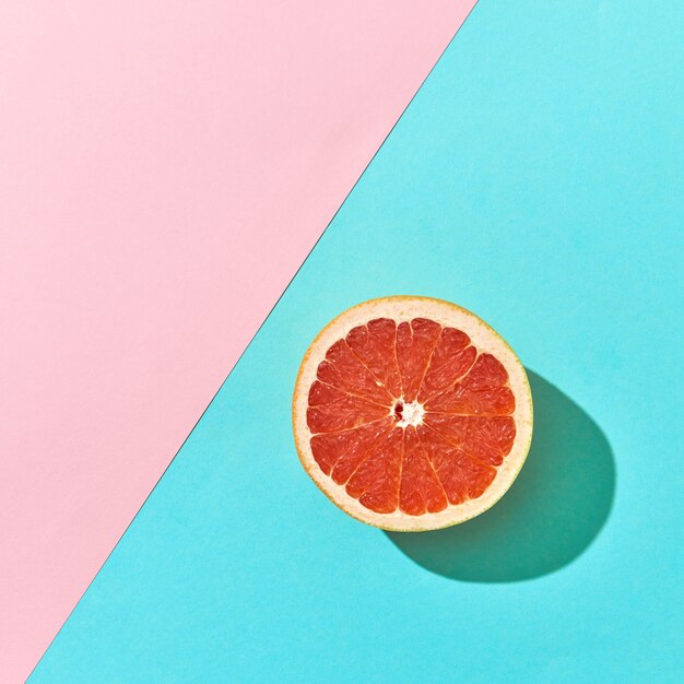 Половина спелого грейпфрута на двойном розовом и синем картонном фоне с пространством для текста. Цитрусовый фрукт. Вид сверху