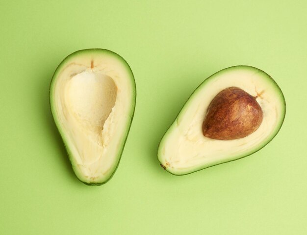 Half ripe green avocado with a brown pit on a green background healthy and tasty fruit