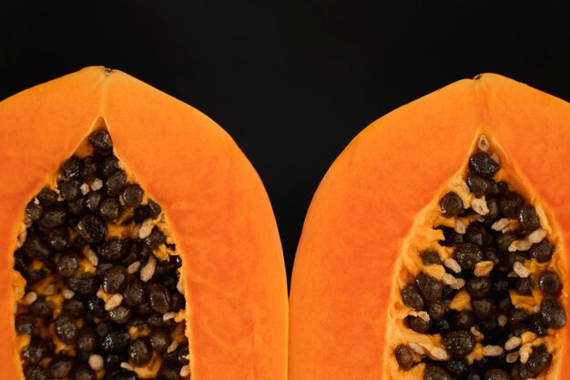 Half of ripe papaya with seed on a black plates and with a green plants on background