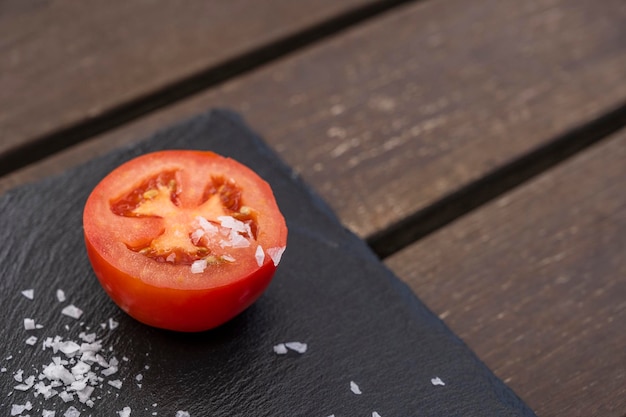 Foto pomodoro mezzo maturo tagliato a metà con scaglie di sale maturo su una tavola di ardesia nera lucida