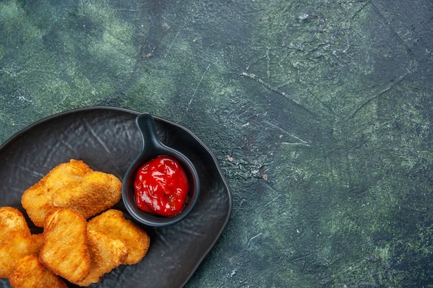 여유 공간이있는 어두운 표면에 검은 접시에 맛있는 치킨 너겟과 케첩의 절반 샷