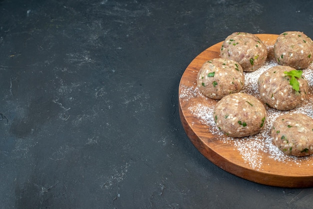 Half shot of uncooked meat balls with green in a brown plate on the right side on black background with free space in side view