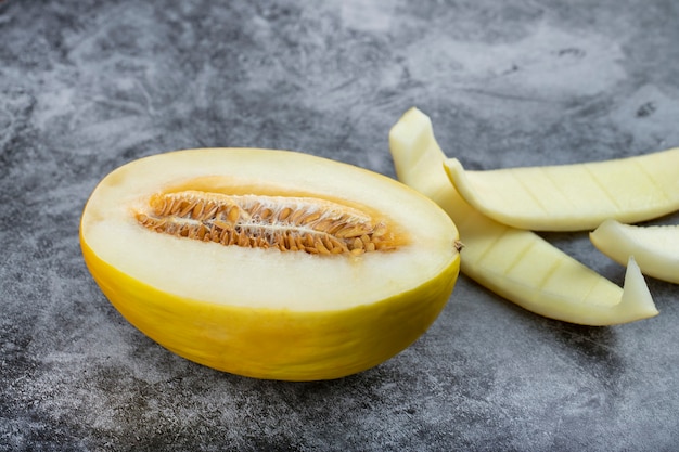 Half sliced honeydew melon with its skin on marble background.