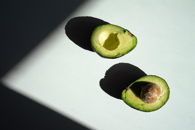 A halfcut avocado lies on the table top view bright sunlight hard shadows from the fruit