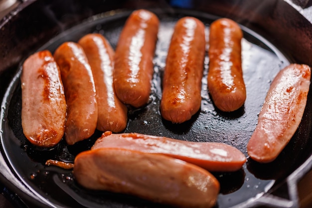 Halfcut sausages are fried in oil in a black cast iron skillet