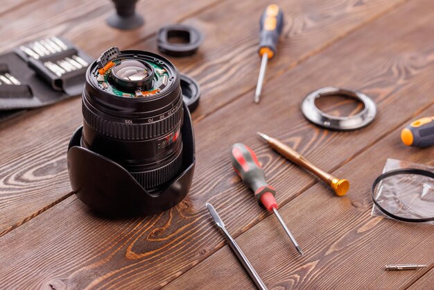 Halfgedemonteerde camerazoomlens op houten tafel omringd met gereedschap