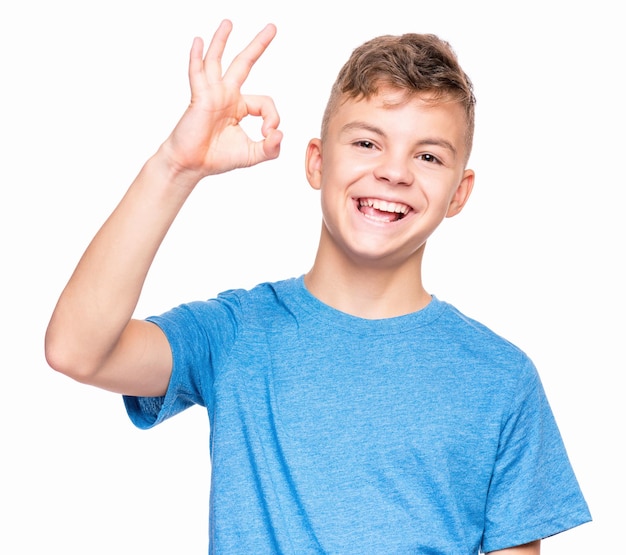 Halflength emotional portrait of caucasian teen boy wearing blue tshirt Funny teenager making ok gesture isolated on white background Handsome child laughing looking very happy