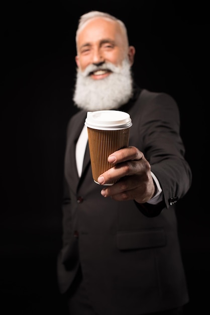 使い捨てのコーヒー カップを保持しているスーツを着た笑顔のビジネスマンの半身像