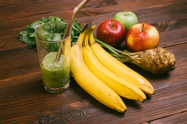 Halfvol glas smoothie met stro, banaan, wortel van selderie en appels op een donkere houten tafel