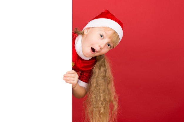 Hallo daar. Meisje jurken in kerst outfit op zoek geschokt van achter een groot leeg bord met copyspace