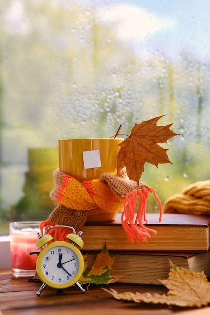 Hallo herfst. Gele wekker, kopje thee op boeken bij het raam, het regent