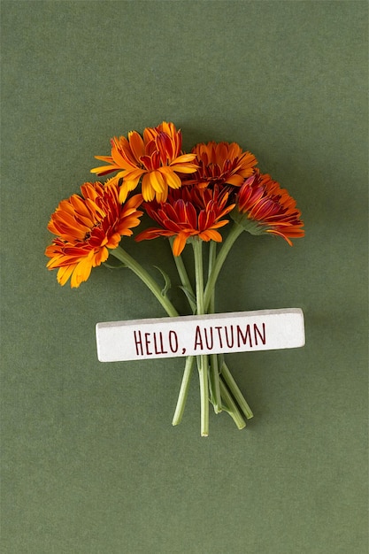 Foto hallo herfst tekst en oranje bloemen op groene achtergrond minimaal concept welkom val bovenaanzicht flat lay wenskaart herfst briefkaart