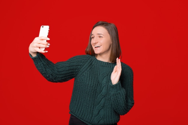 Hallo! portret van vriendelijk meisje hallo gebaar zwaaien en videogesprek voeren op mobiele telefoon, staande over rd geïsoleerde achtergrond